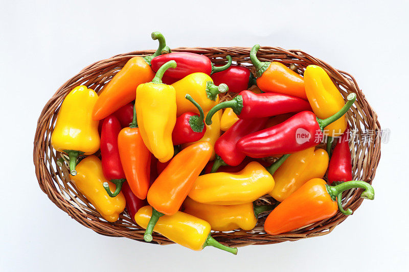 一堆红色、黄色和橙色的迷你辣椒(Capsicum annuum)的特写图片，白色背景上的柳条篮子里有绿色的茎